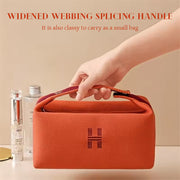Close-up of eprolo's orange canvas makeup bag being held, showcasing the widened webbing handle and stylish design ideal for carrying cosmetics.
