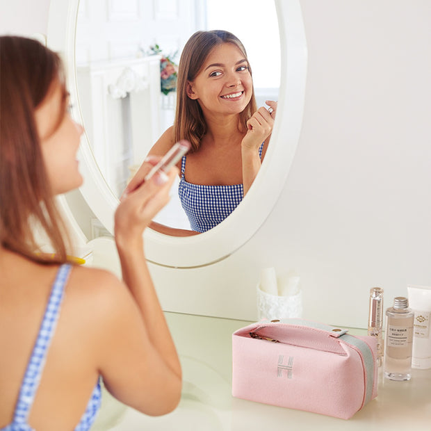 Pink canvas makeup bag from eprolo featured on a vanity with beauty products, highlighting its trendy aesthetic and spacious interior for organization.